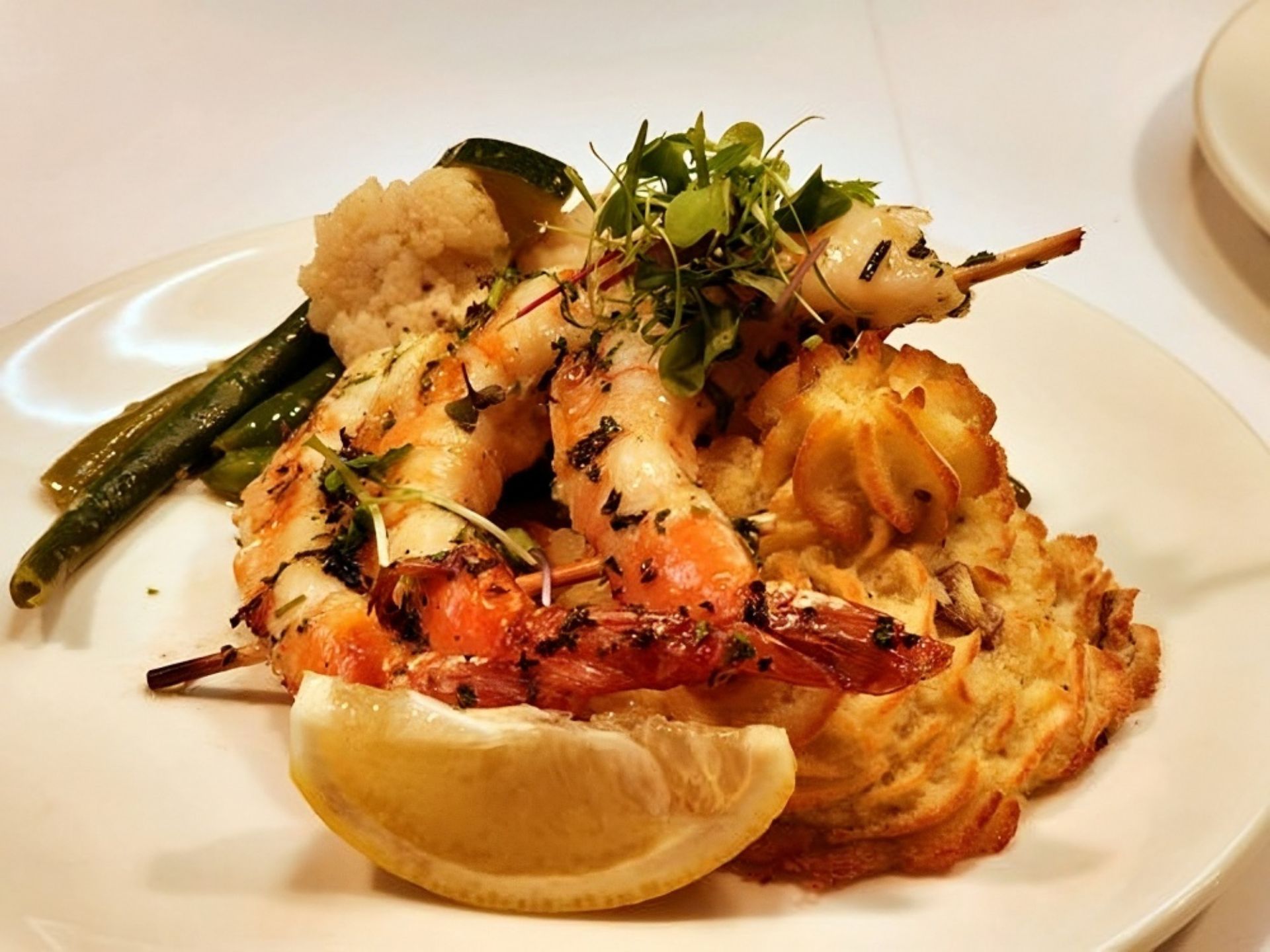 Grilled shrimp skewers garnished with herbs, served on piped mashed potatoes with green beans, cauliflower, and a lemon wedge—an elegant dish enjoyed at MorningStar Senior Living Kirkland for exceptional retirement living.