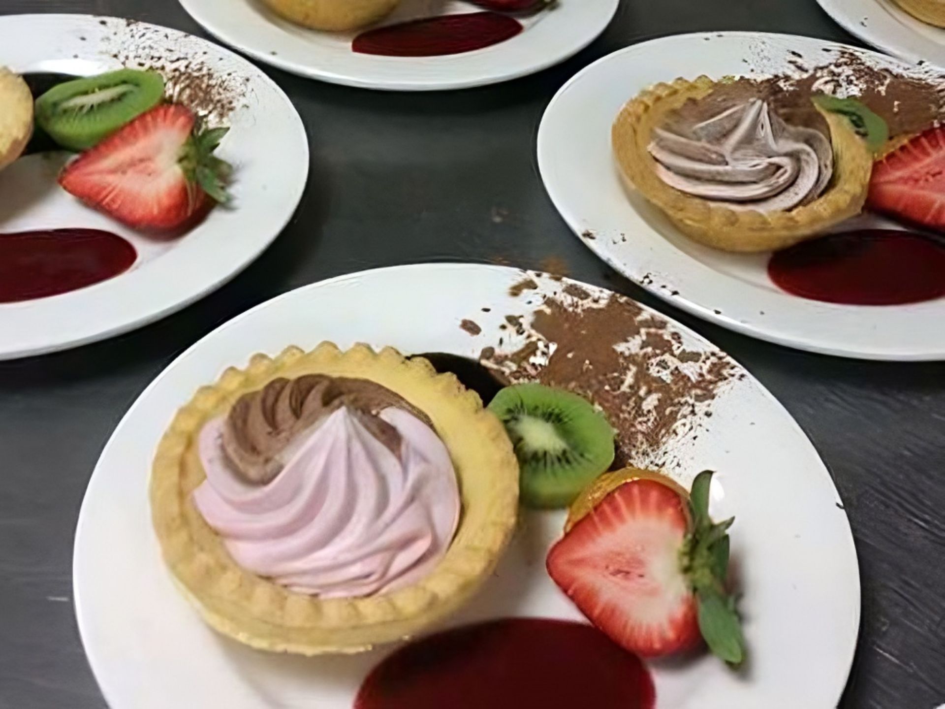 At MorningStar Senior Living Kirkland, plates each hold a tart topped with swirled chocolate and berry cream, garnished with sliced strawberries, kiwi, a smear of red sauce, and a dusting of cocoa powder—delighting those enjoying retirement living.