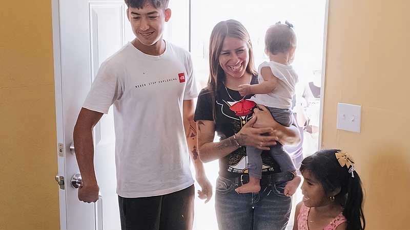A smiling woman holding a baby enters a brightly lit room at MorningStar Senior Living Kirkland with a young man and a little girl, all appearing happy and excited, capturing the joy of retirement living together.
