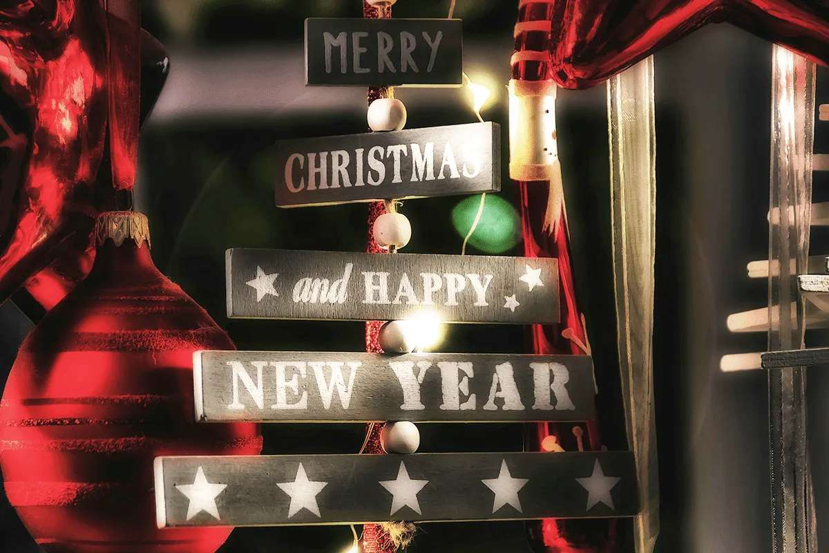 Wooden signs shaped like a Christmas tree read “Merry Christmas and Happy New Year,” with strings of white beads and festive red decorations in the background. Warm lights create a cozy holiday atmosphere at MorningStar Senior Living Kirkland.