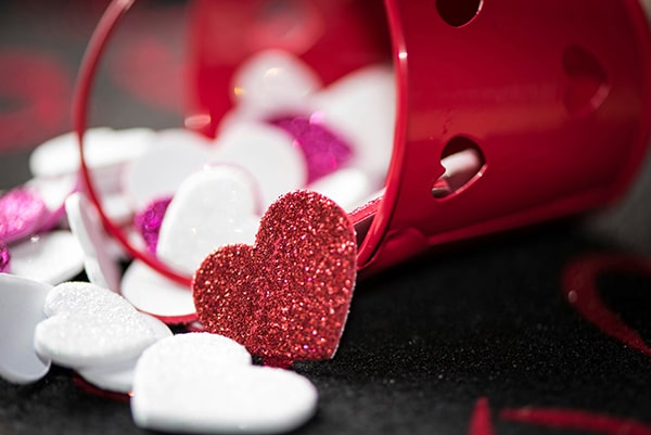 A small red bucket tipped over, spilling out glittery red, white, and pink heart-shaped decorations onto a black surface—perfect for celebrating Retirement Living at MorningStar Senior Living Kirkland.