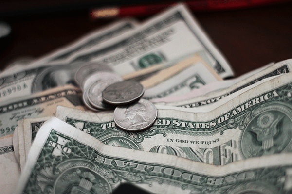 Close-up of various U.S. dollar bills and coins, including one-dollar bills and quarters, arranged in a scattered manner on a dark surface at MorningStar Senior Living Kirkland, emphasizing financial aspects of retirement living.