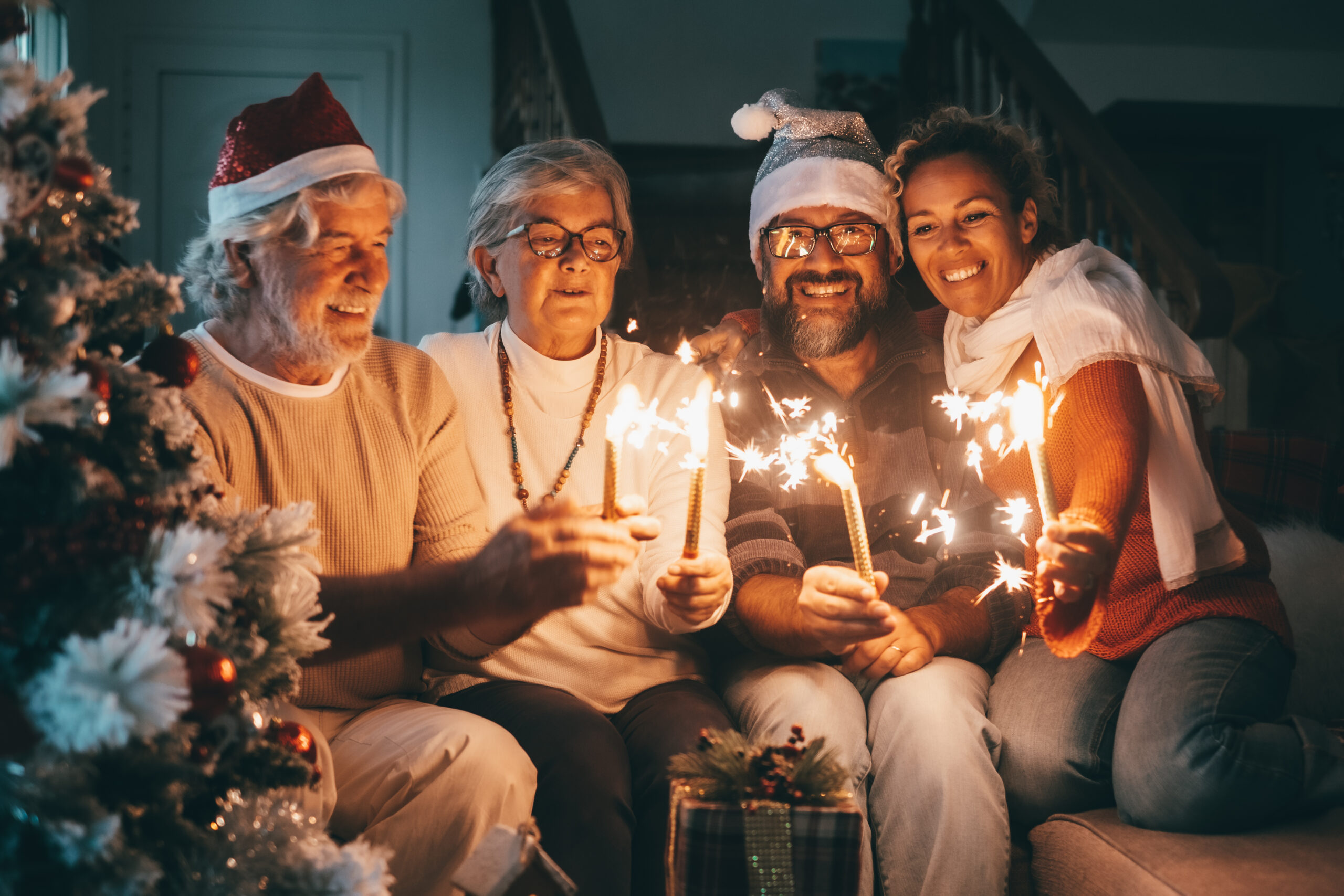 Happy family group of senior parents and middle aged son with wi A group of smiling seniors holding sparklers and wearing Santa hats